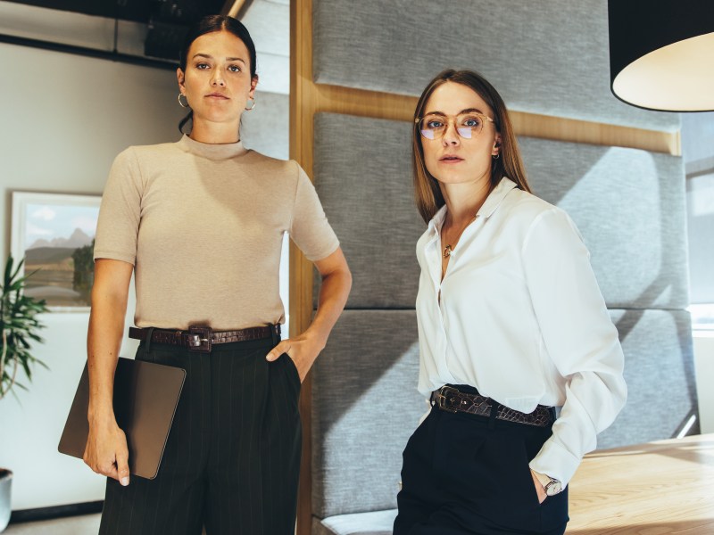 Junge Geschäftsfrauen schauen in die Kamera, während sie in einem Büro stehen.