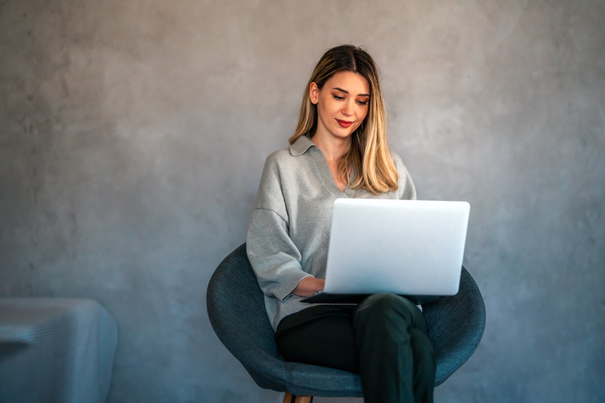 Eine lächelnde junge Frau, die einen Laptop benutzt.