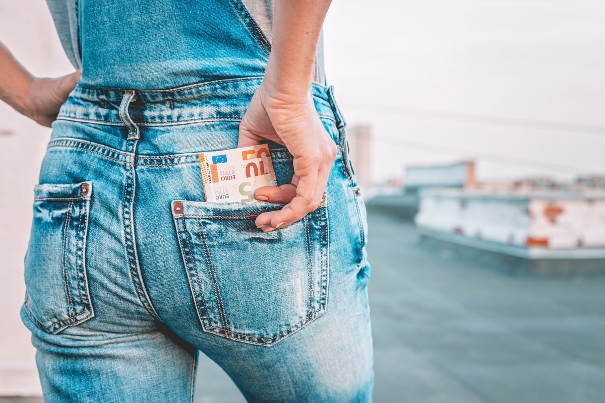 Die Hand einer Frau holt Euro-Scheine aus der Gesäßtasche ihrer Jeans.