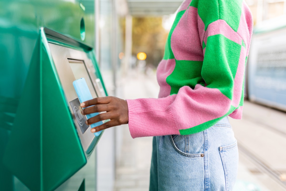 Frau in pink, grünen Pullover hebt Geld ab.