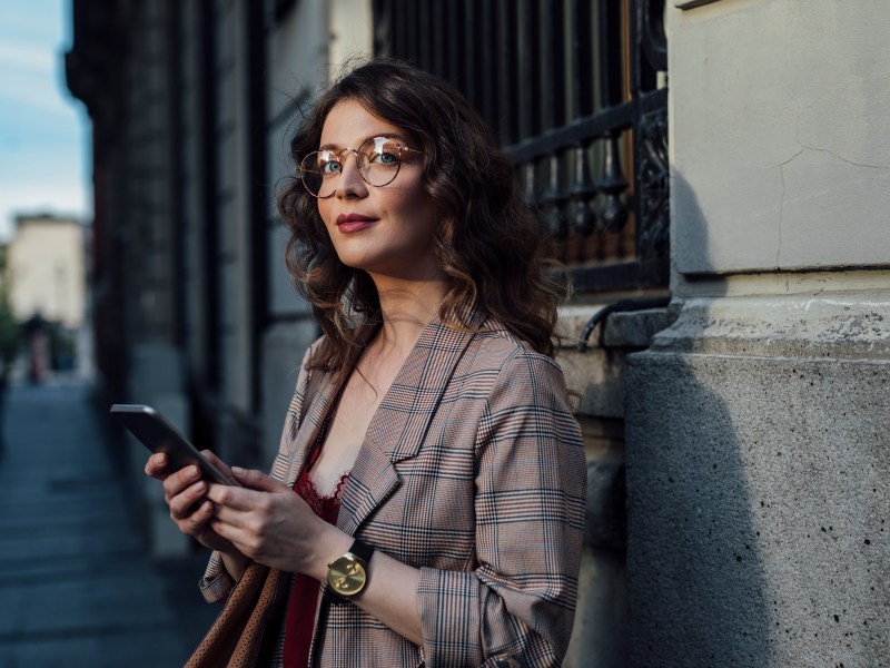 Eine elegante Frau steht auf der Straße und hält ihr Telefon in der Hand.