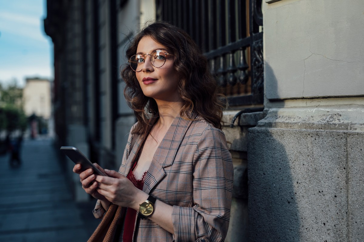 Eine elegante Frau steht auf der Straße und hält ihr Telefon in der Hand.