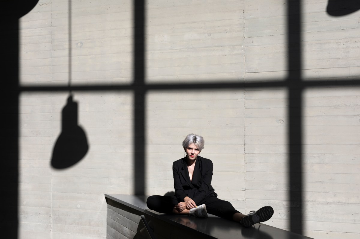 Frau im eleganten schwarzen Kleid mit Wand mit Schatten im Hintergrund.