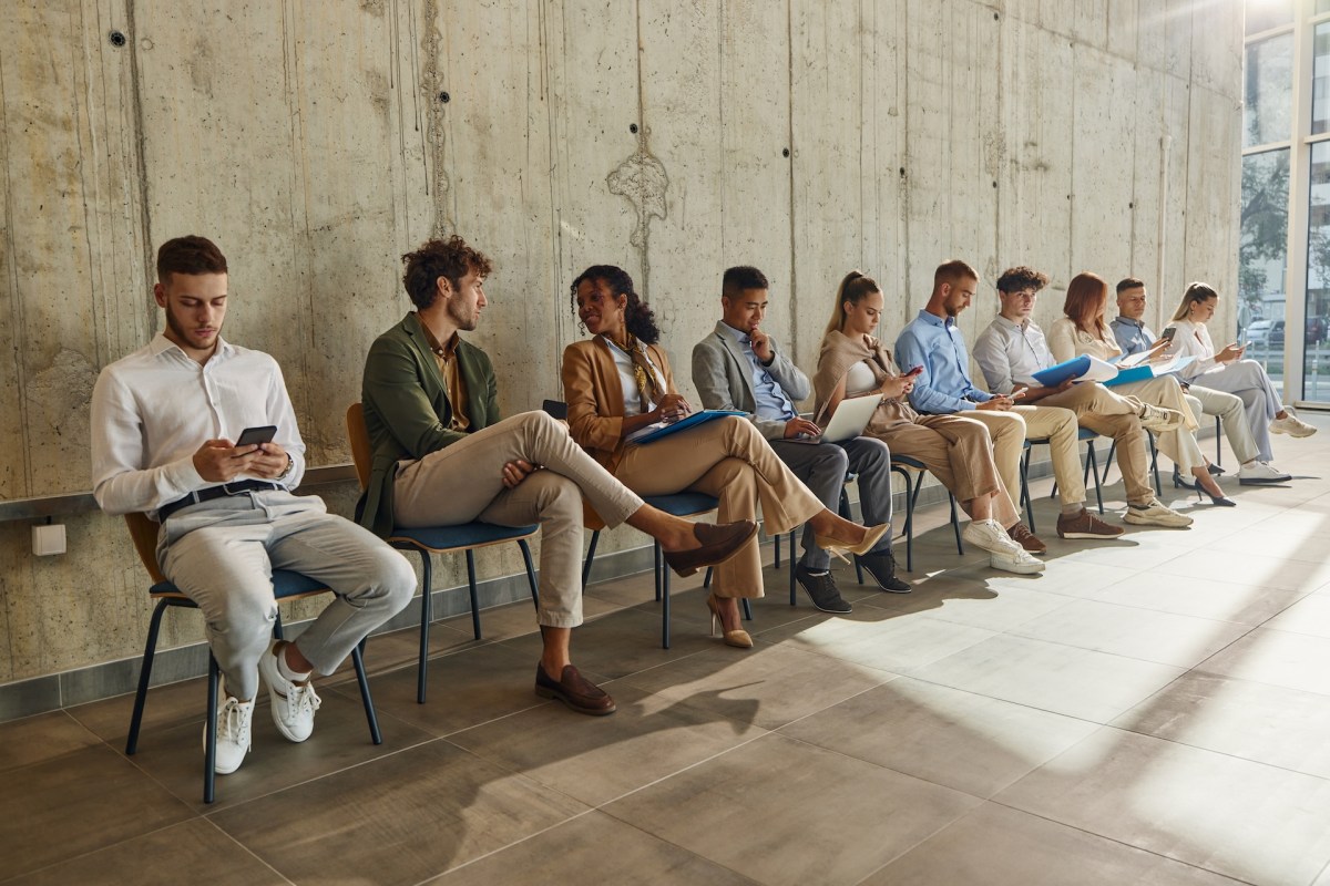 Große Gruppe von Bewerber:innen wartet in einem Flur auf ein Vorstellungsgespräch