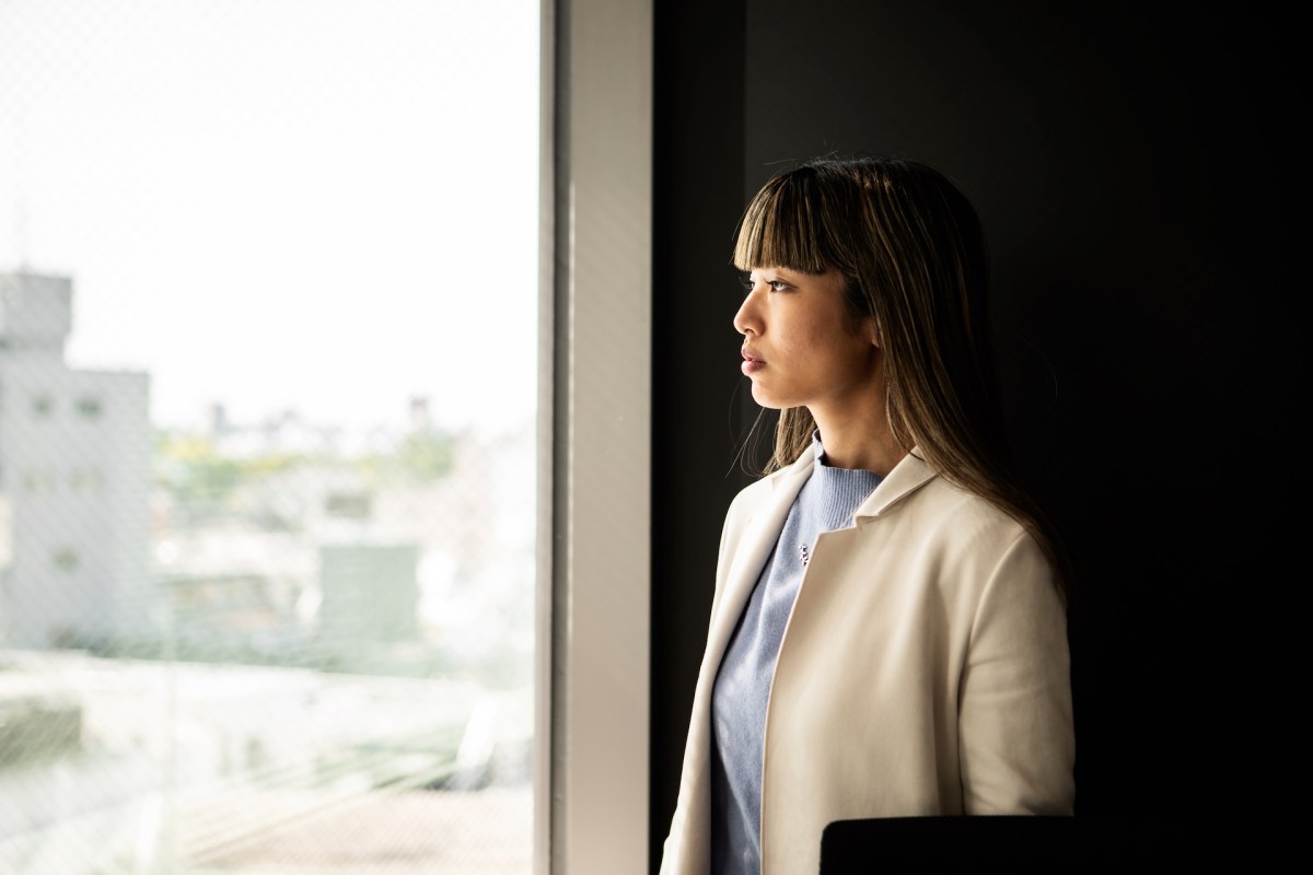 Eine Frau im beigen Anzug schaut im Büro aus dem Fenster.
