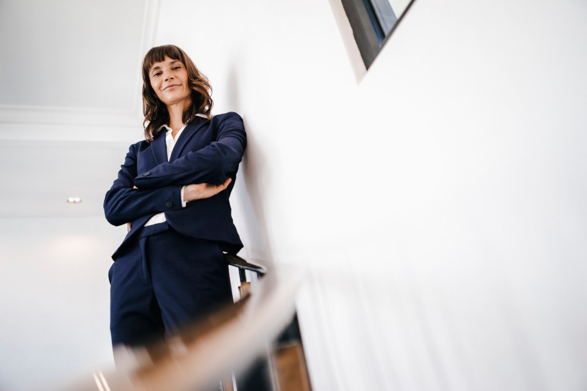 Eine Frau im Anzug schaut mit verschränkten Armen die Treppe hinunter.