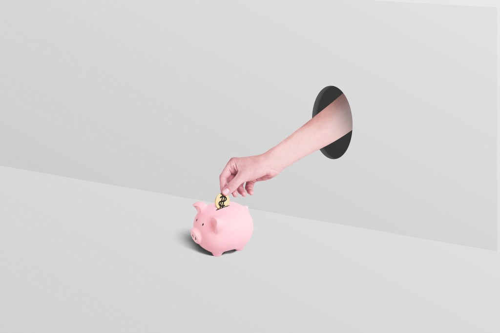 Eine Hand greift durch ein Loch und wirft eine Münze in ein Sparschwein.