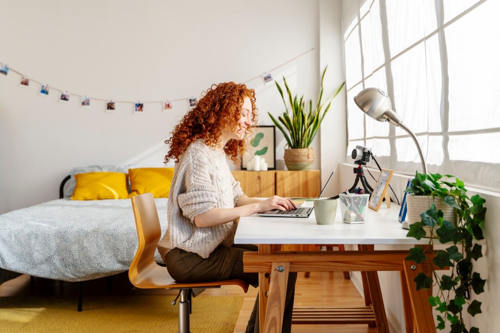 Eine junge Frau sitzt in ihrem Zimmer am Schreibtisch und übt am Laptop.