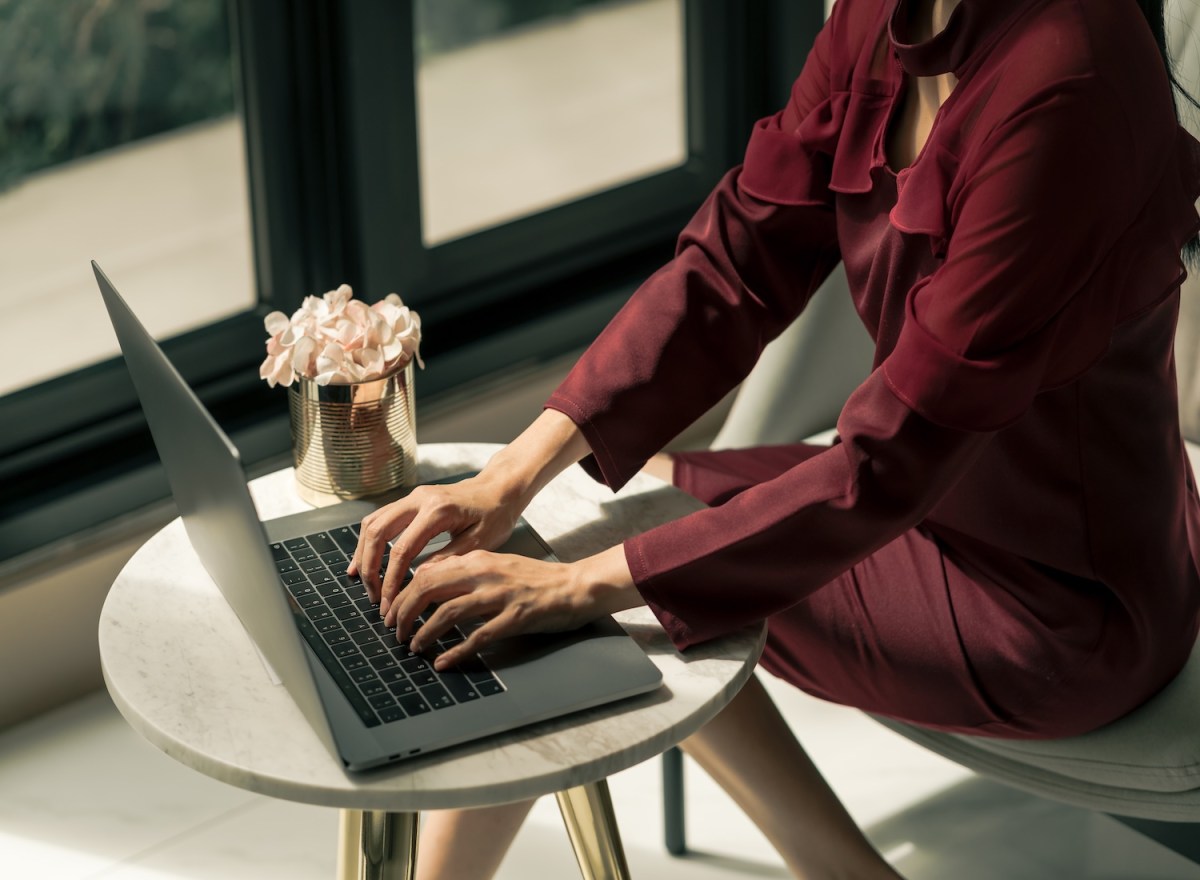 Eine Frau im roten Kleid tippt auf dem Laptop.
