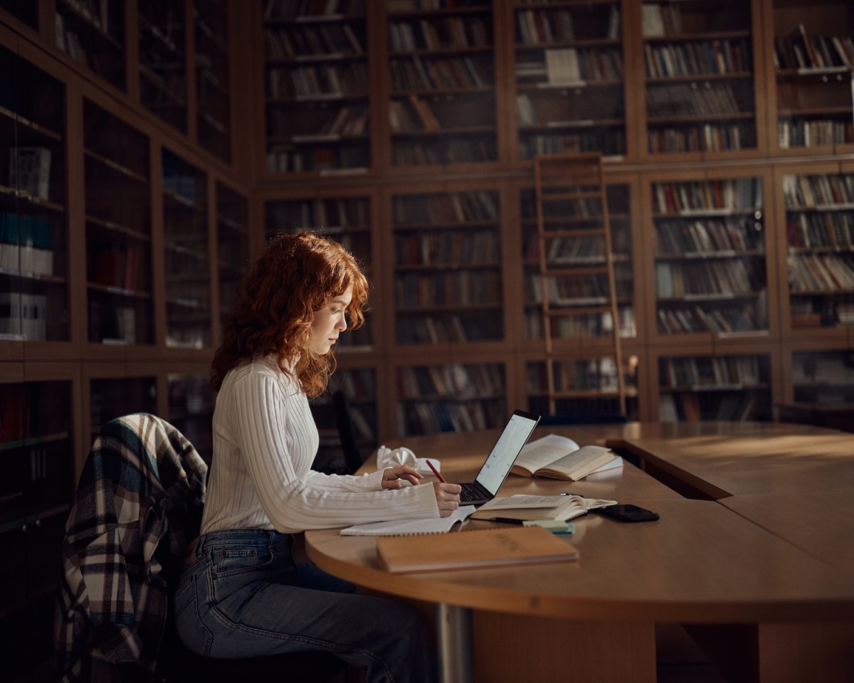 Eine Studentin macht sich Notizen, während sie in der Bibliothek einen Computer benutzt.
