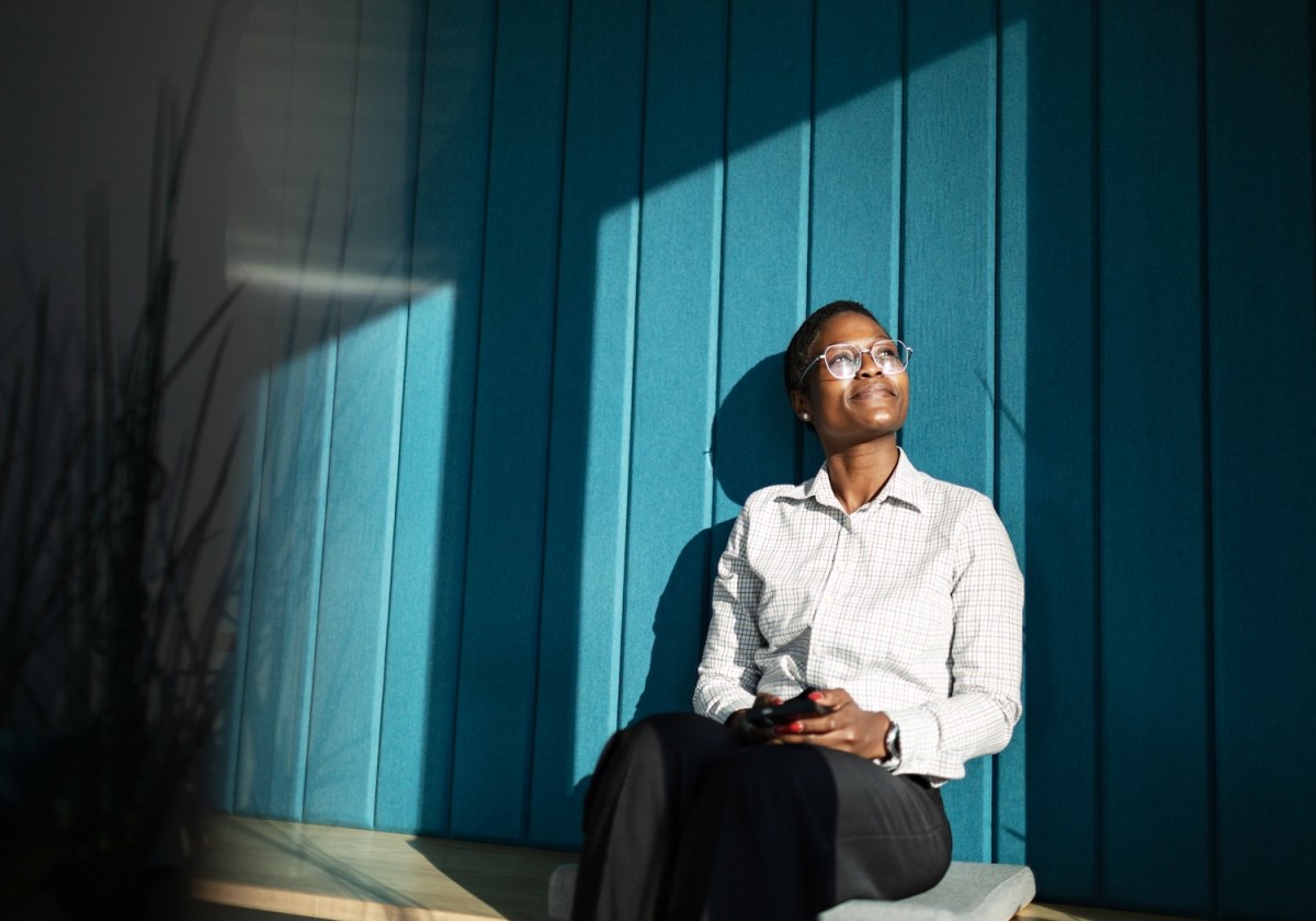 Junge erwachsene schwarze Frau sitzt im Büro, lächelt und entspannt.